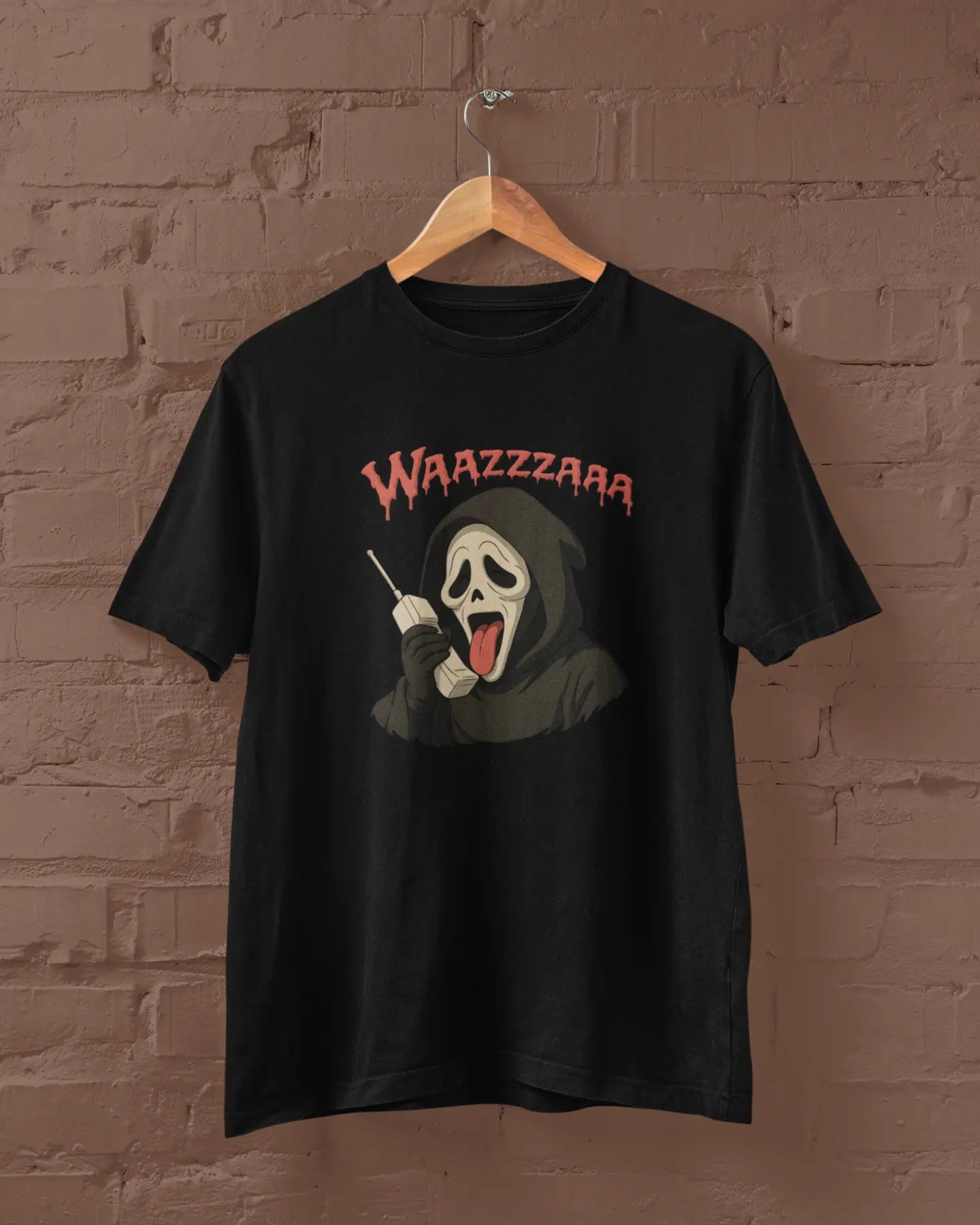 Black t-shirt with a graphic design of a character and 'WAZZZAAA' text, hanging on a brick wall.