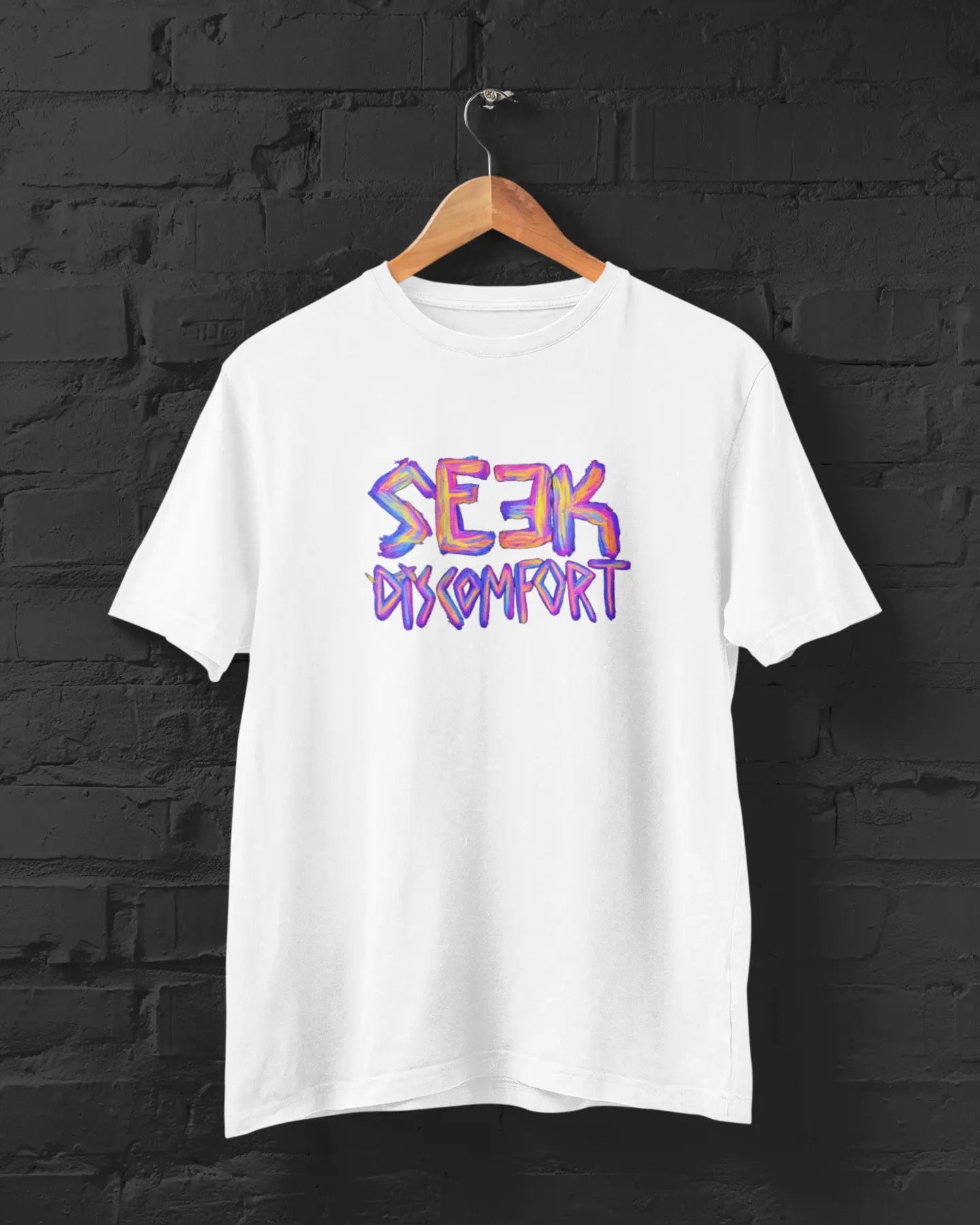 White t-shirt with 'Seek Comfort' text in colorful letters on a black brick wall background.