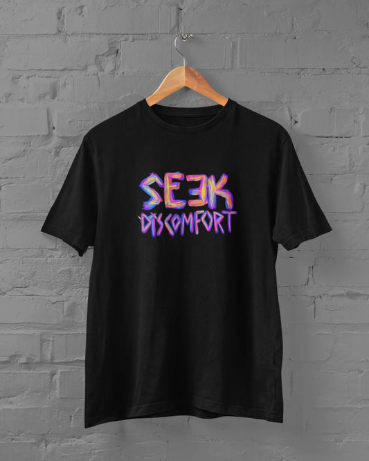 Black t-shirt with 'Seek Discomfort' text on a hanger against a gray brick wall.