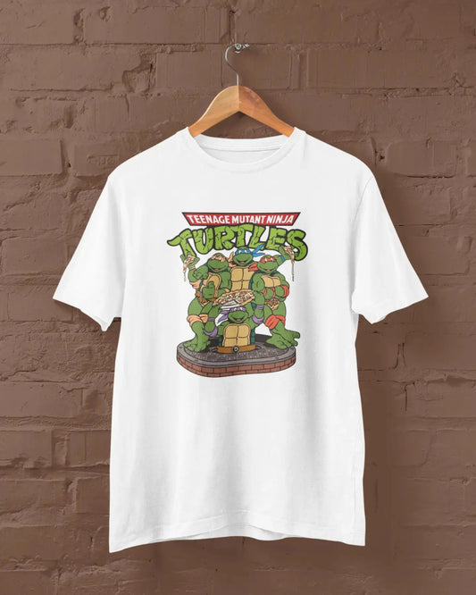 White t-shirt with Teenage Mutant Ninja Turtles graphic on a hanger against a brown brick wall.
