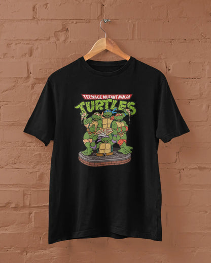 Black t-shirt with Teenage Mutant Ninja Turtles graphic on a hanger against a brick wall.
