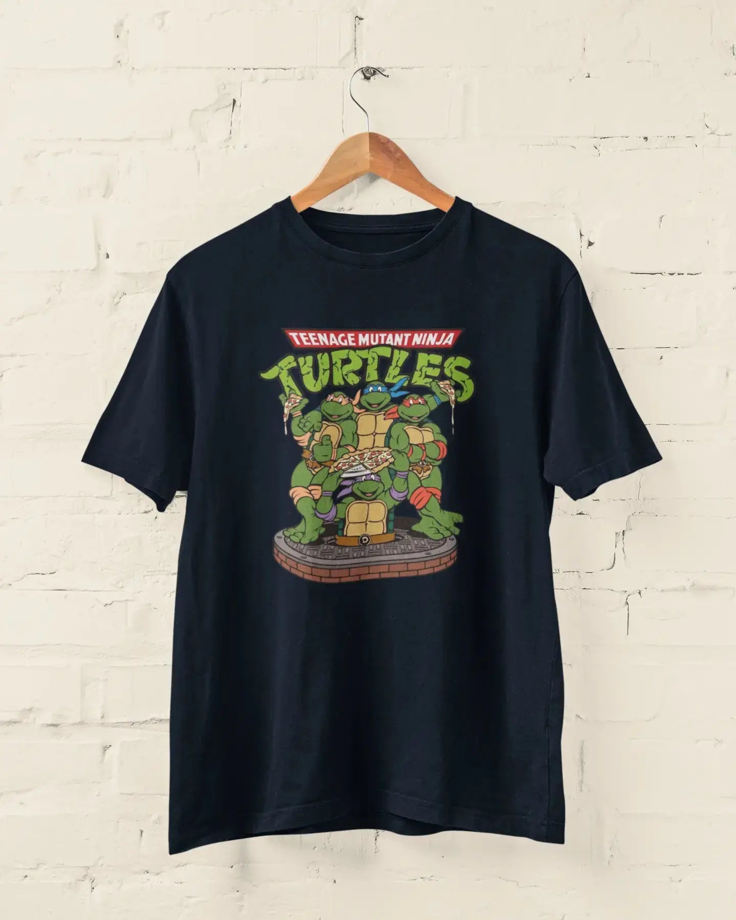 Navy Blue t-shirt with Teenage Mutant Ninja Turtles graphic on a hanger against a white brick wall.