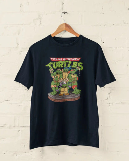 Navy Blue t-shirt with Teenage Mutant Ninja Turtles graphic on a hanger against a white brick wall.