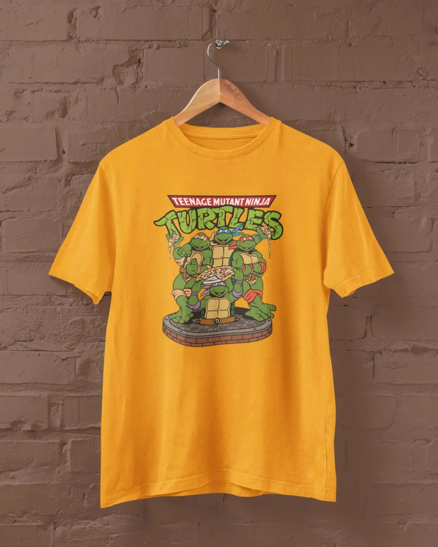 Yellow t-shirt with Teenage Mutant Ninja Turtles graphic on a hanger against a brick wall.