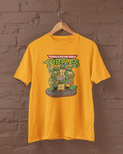 Yellow t-shirt with Teenage Mutant Ninja Turtles graphic on a hanger against a brick wall.