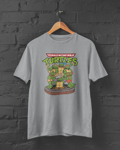 Gray t-shirt with Teenage Mutant Ninja Turtles graphic on a hanger against a brick wall.