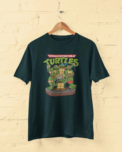 Petrol blue t-shirt with Teenage Mutant Ninja Turtles graphic on a wooden hanger against a beige brick wall.