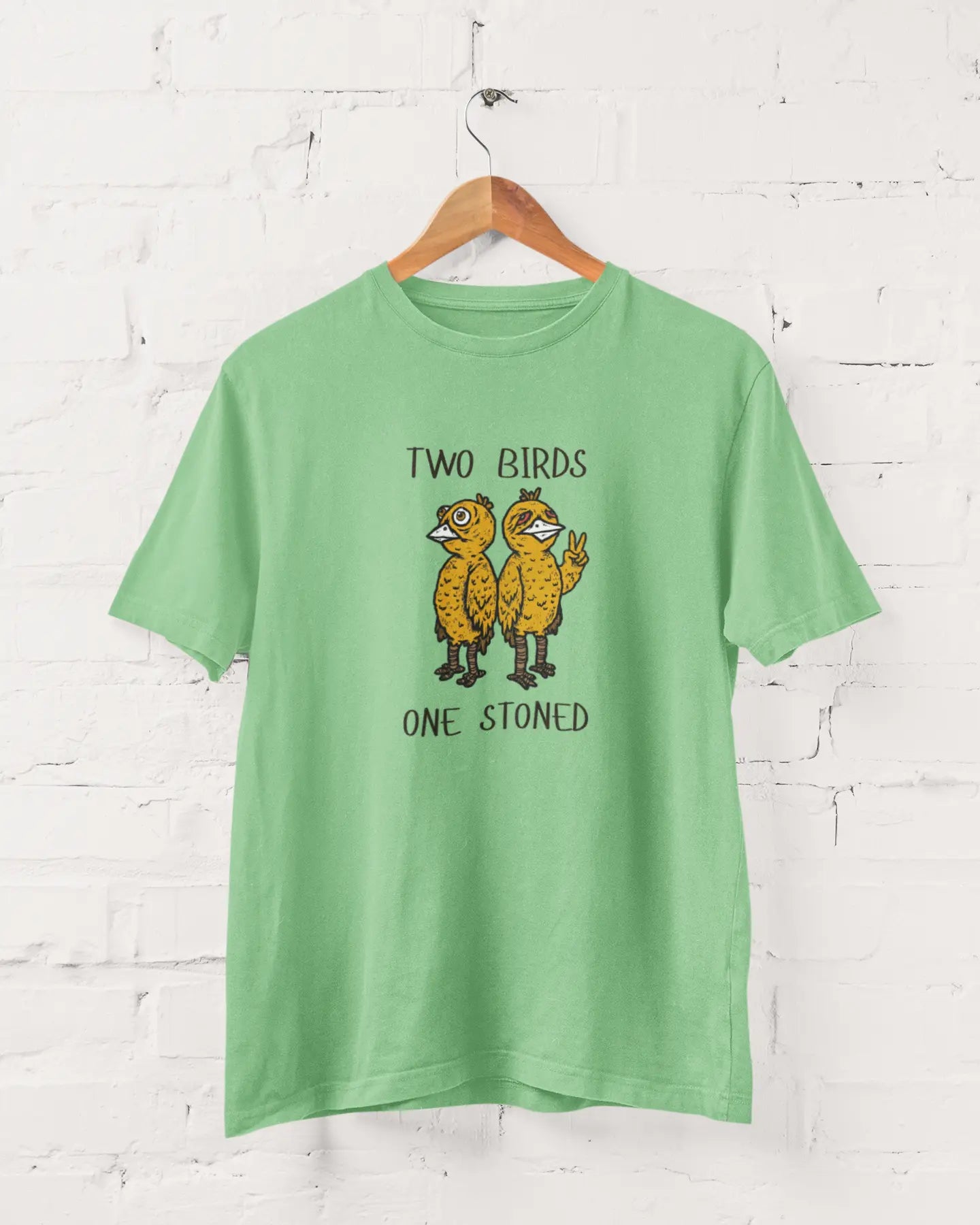 Green t-shirt with 'Two Birds One Stoned' graphic on a white brick wall background